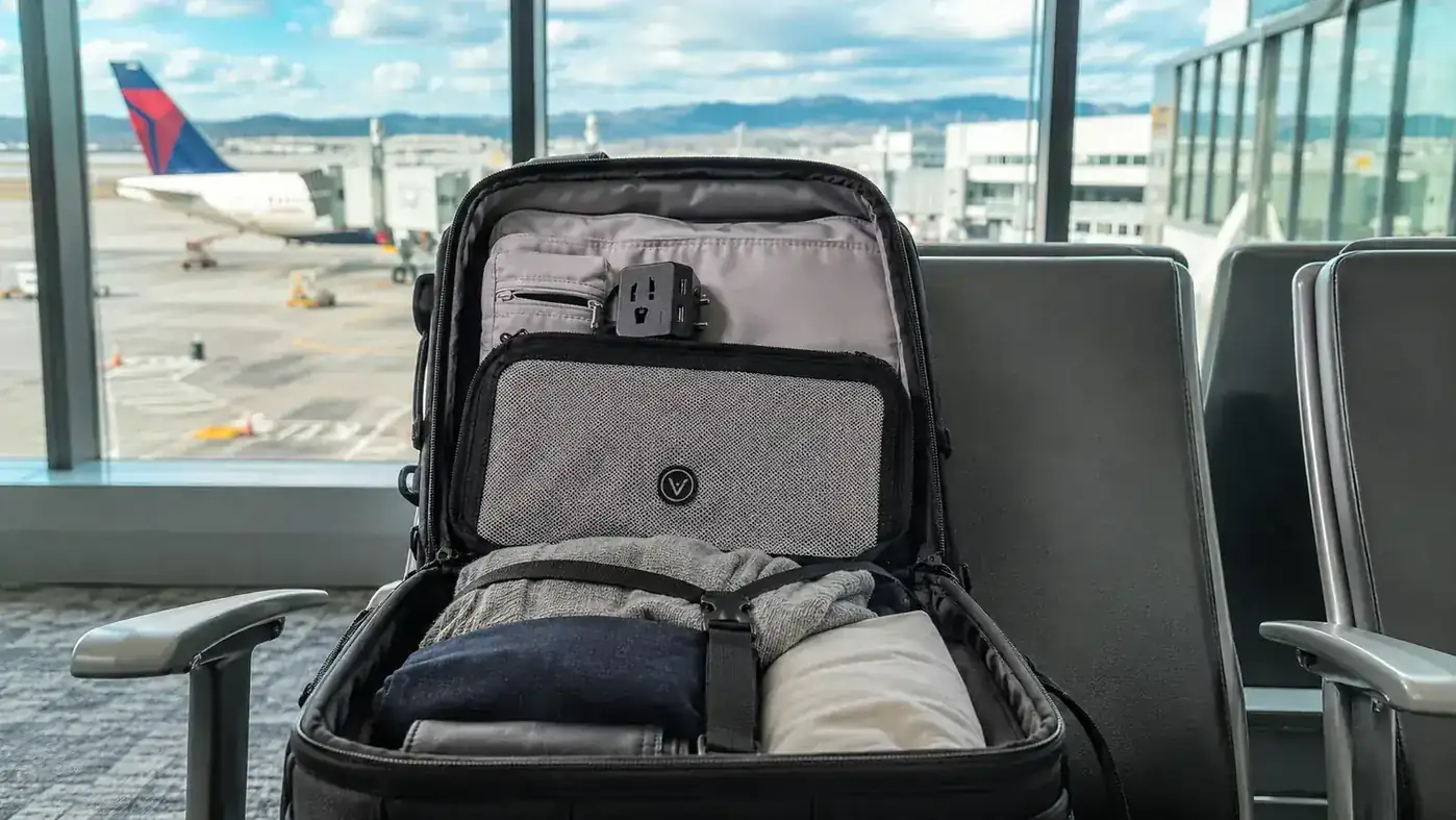 Compact universal travel adapter resting on top of a packed carry-on bag near an airport departure gate window