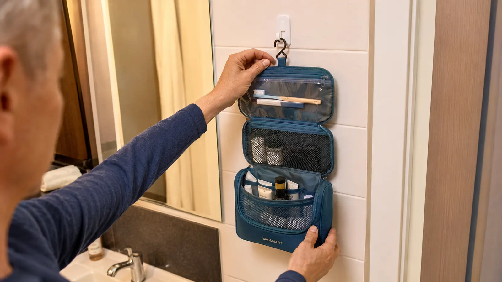 Hands unpacking the BAGSMART toiletry bag and setting it on a hook inside a cramped hostel bathroom