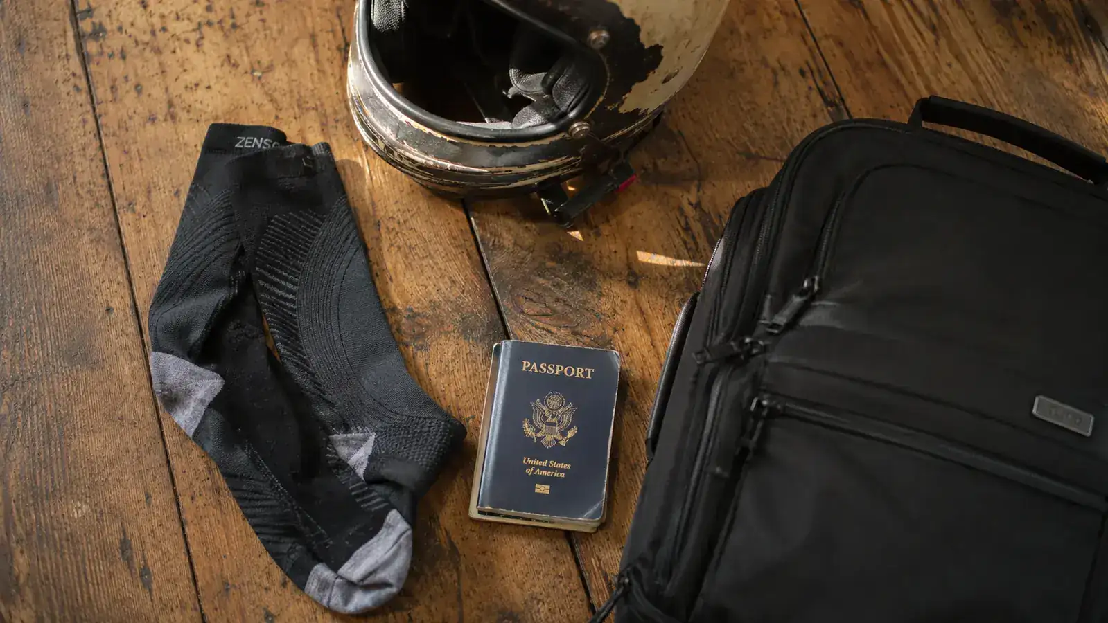 Traveler packing compression socks into a carry-on bag beside a motorcycle helmet and passport