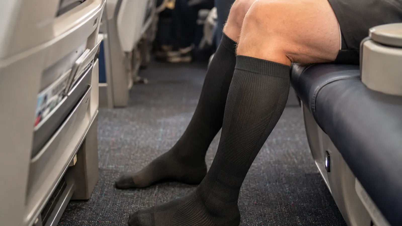 Ankles and feet of a traveler visible in an airplane aisle, wearing black compression socks, no visible swelling