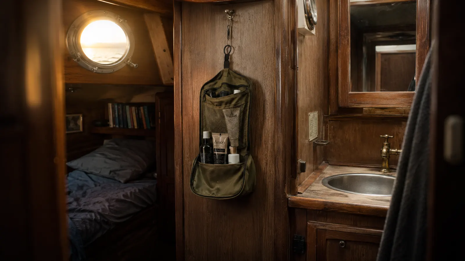 A sailboat galley with soft morning light, a worn travel bag hanging from a towel bar near the porthole